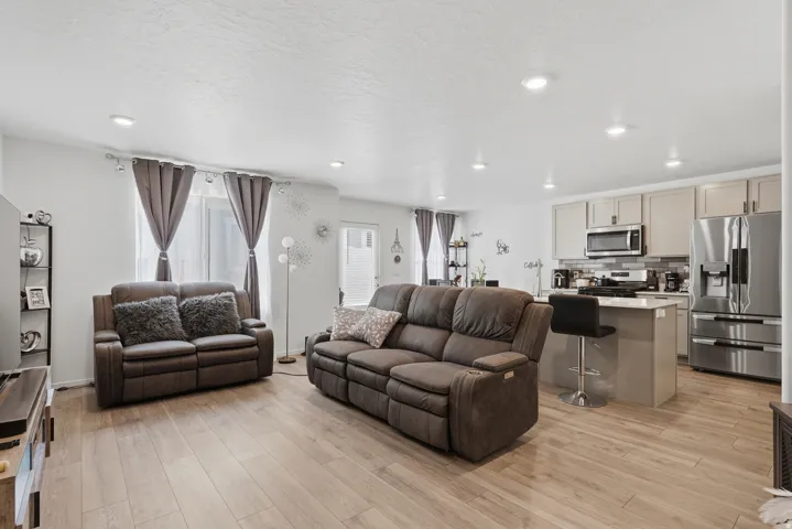 Open-concept living area featuring wood-finish flooring, recessed lighting, and a kitchen with light-toned cabinetry, stainless steel appliances, and an island with bar seating