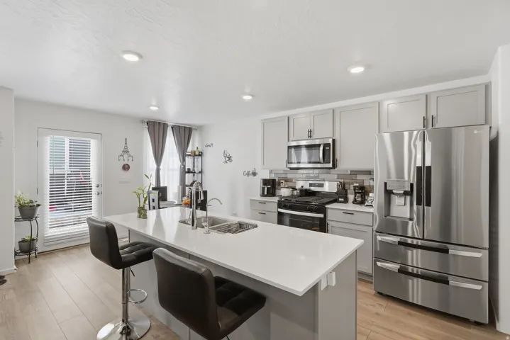 Contemporary kitchen featuring a large island with sink, light-toned cabinetry, stainless steel appliances, and wood-finish flooring