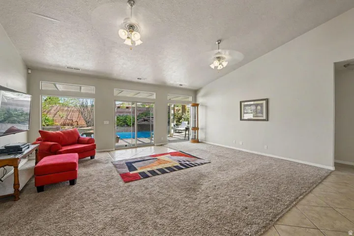 Spacious living area featuring vaulted ceilings, a combination of carpeting and tile flooring, and multiple windows with upper transoms