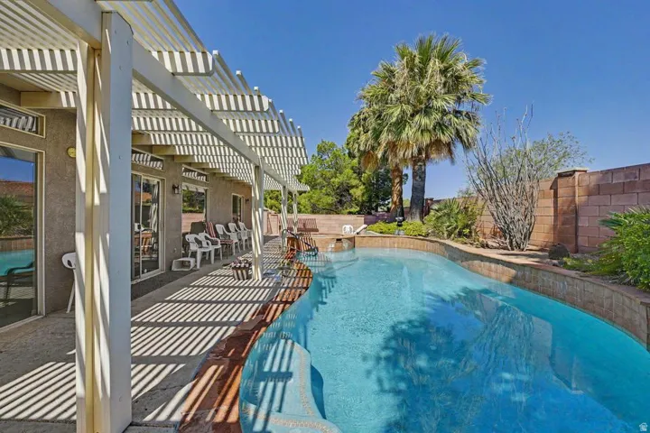 Curved swimming pool with an integrated spa, surrounded by a paved patio and a detached pergola structure