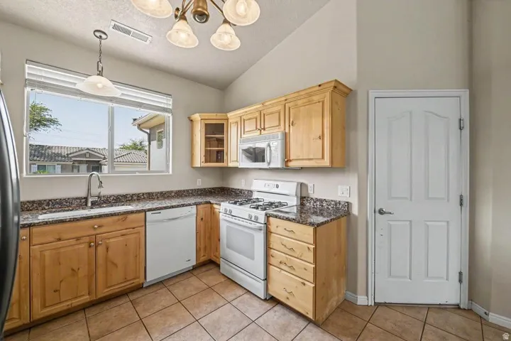 Kitchen featuring natural wood cabinetry, granite-finish countertops, tile flooring, and a white appliance package including a gas range, dishwasher, and microwave