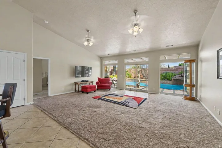 Spacious living area featuring vaulted ceilings, ceiling fans, and a combination of tile and plush carpet flooring