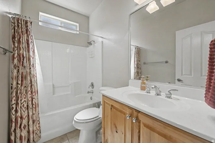 Bathroom featuring a built-in tub with shower, single vanity with light wood cabinetry, white countertop, and an overhead window