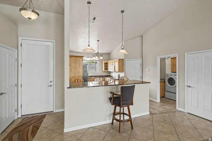 Kitchen bar featuring a stone-finish countertop, pendant lighting, and light wood-finish cabinetry