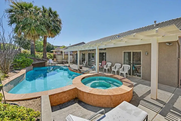 Backyard featuring a freeform swimming pool with integrated spa and water feature, along with a covered patio area