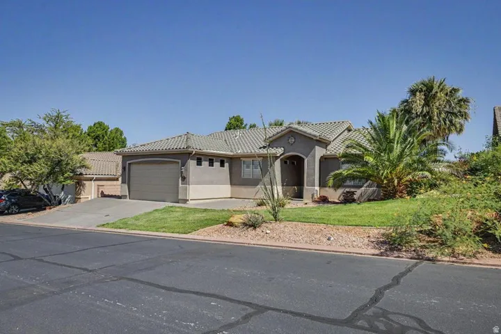 Stucco exterior with a tiled roof, featuring an arched entry, an attached garage, and desert landscaping with palm trees