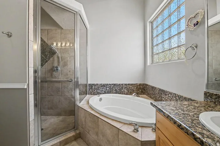 Bathroom featuring an alcove bathtub, a walk-in shower with glass enclosure, granite countertops, tile flooring, and a glass block window
