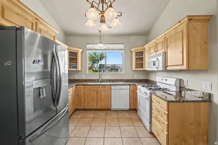 Kitchen featuring wood-finish cabinetry, granite countertops, stainless steel refrigerator, white gas range, and tile flooring