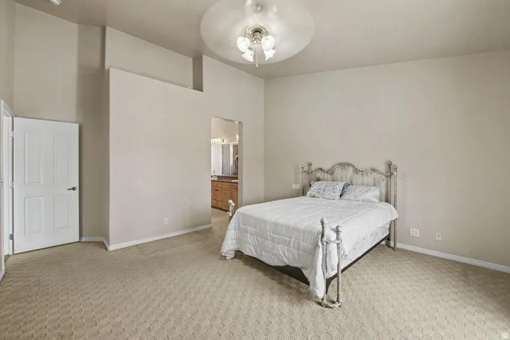 Carpeted bedroom featuring a tray ceiling with a built-in fan light fixture, a paneled door, and an open doorway revealing a bathroom vanity with a wood-finish cabinet and countertop