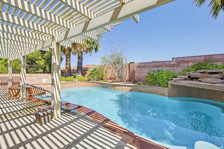 Outdoor space featuring a pergola-covered patio, a kidney-shaped pool with integrated spa, a stone waterfall feature, and a block wall perimeter