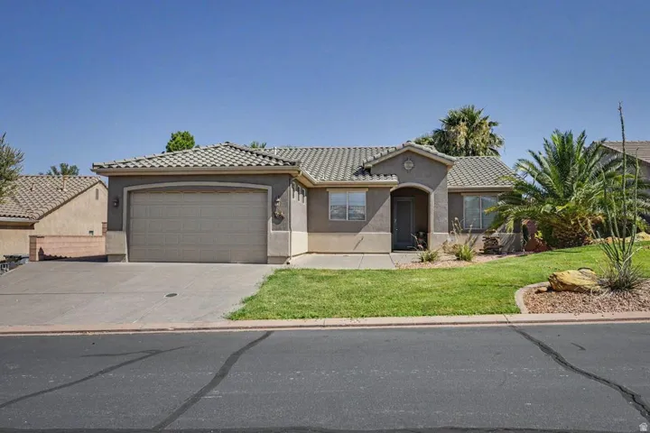 Stucco exterior with a tiled roof, an arched entry, a two-car garage, and desert-adapted landscaping