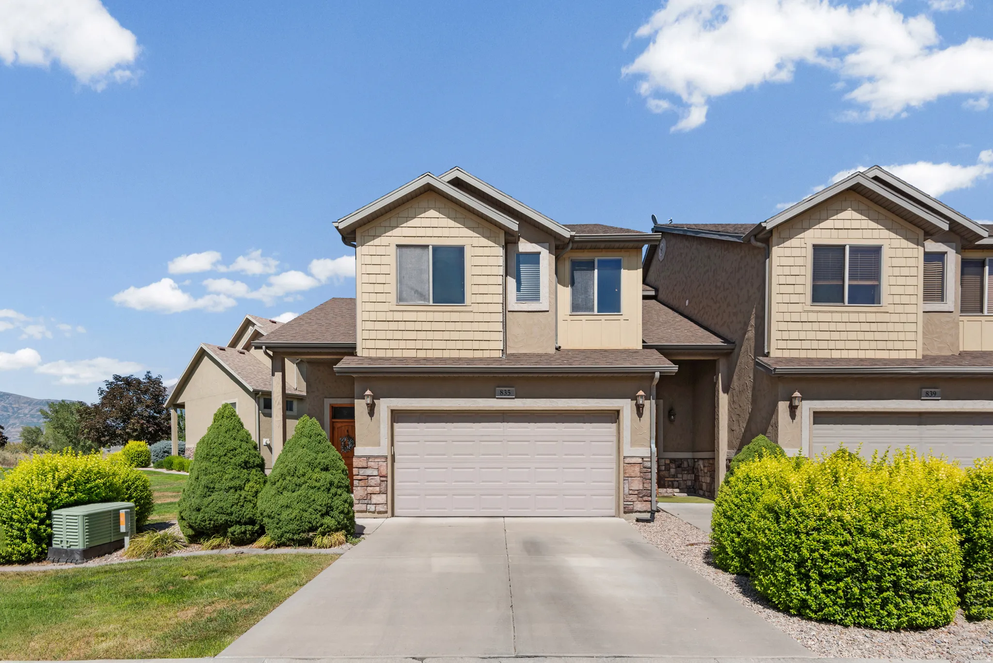 Multi-level exterior featuring tan siding, stacked stone accents, a beige garage door, and a concrete driveway