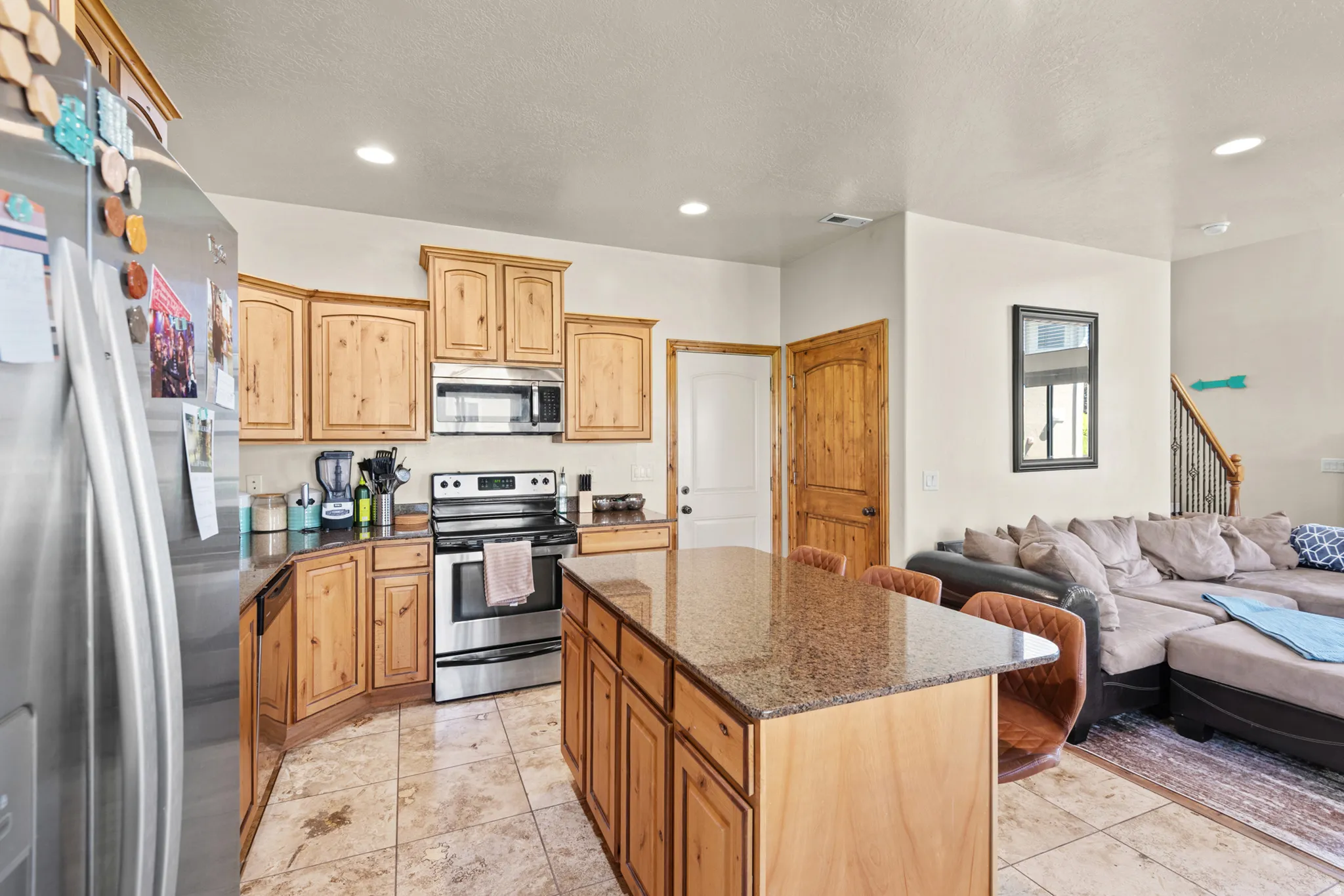 Open-concept kitchen featuring wood cabinetry, stainless steel appliances, a center island with bar seating, and tile flooring