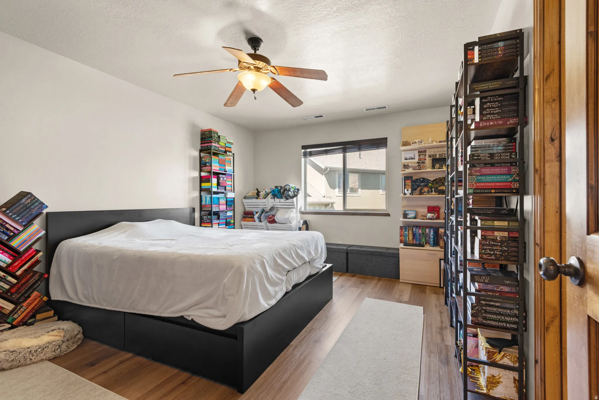 Bedroom featuring wood-finish flooring, a ceiling fan with integrated lighting, a window with blinds, and built-in shelving