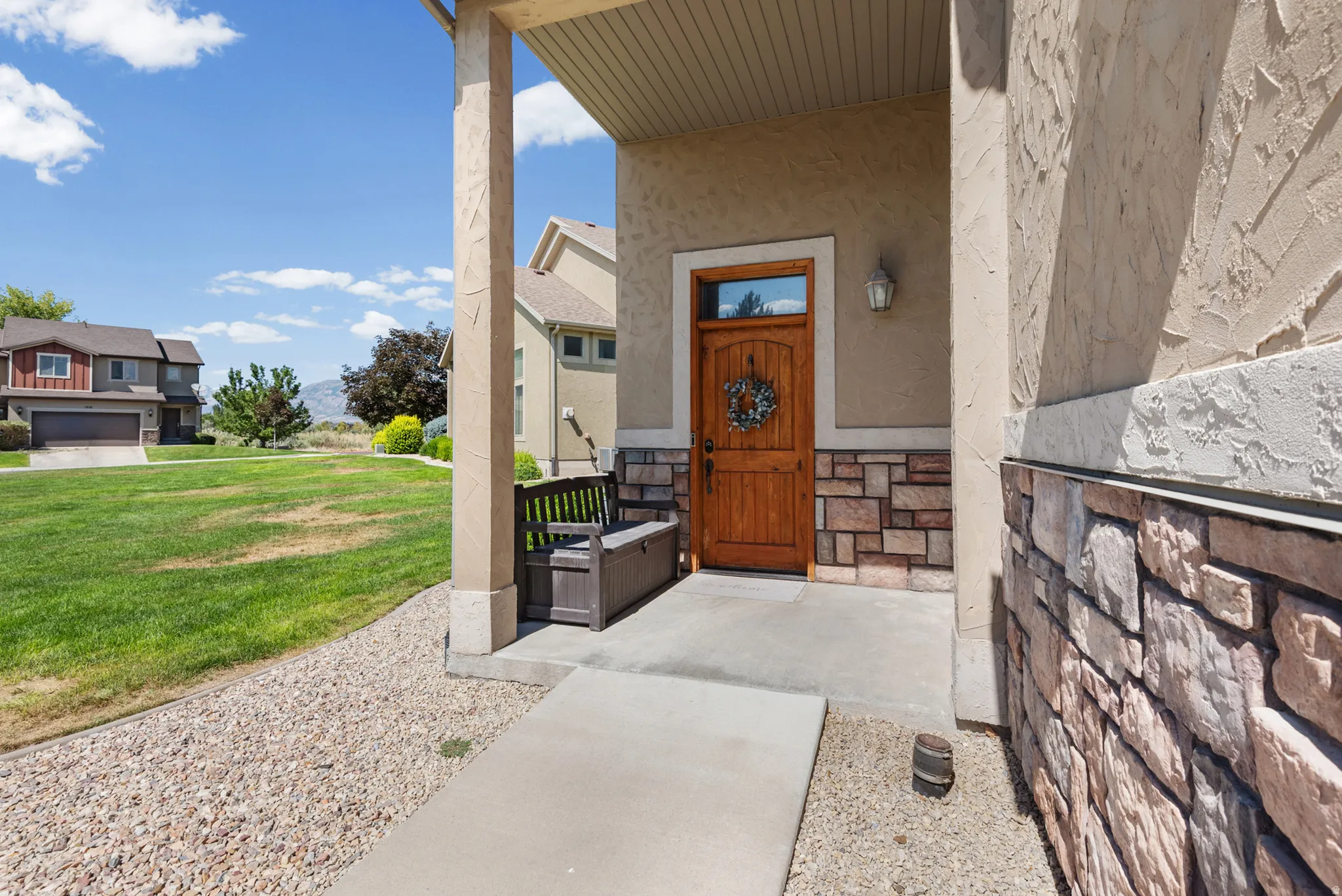 Inviting entryway featuring a wooden front door, stone veneer accents, stucco siding, and a covered porch with column supports