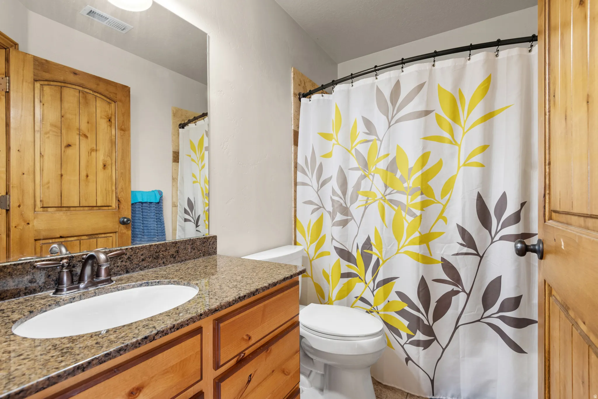 Bathroom featuring a wood-finish vanity with an oval undermount sink, a speckled stone-finish countertop, and a brushed nickel faucet