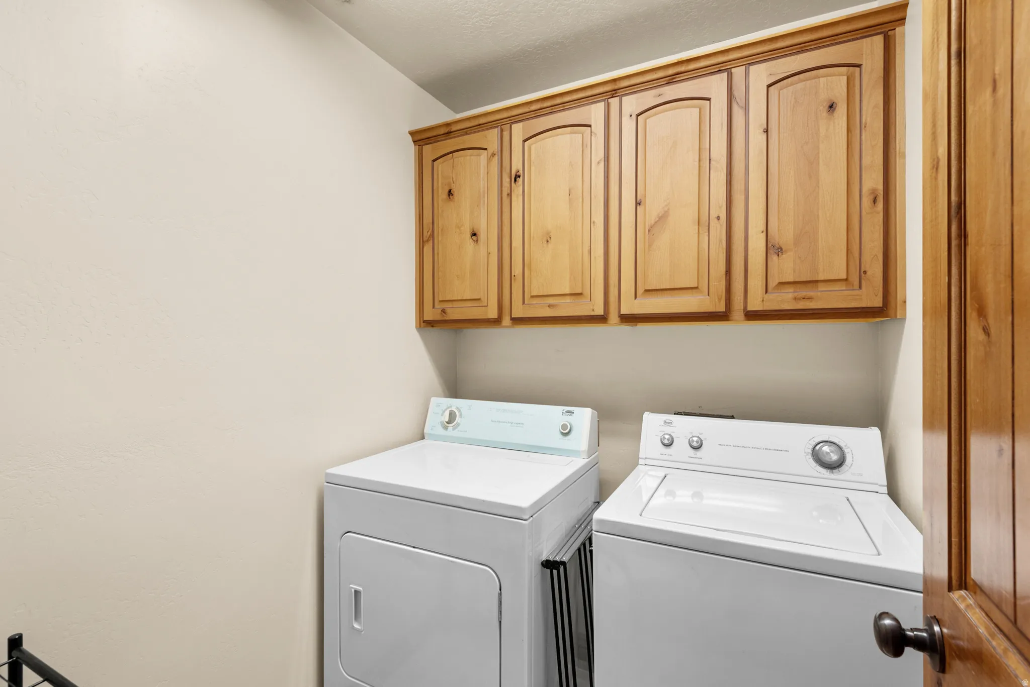 Laundry area featuring wood cabinetry, overhead storage, and white walls