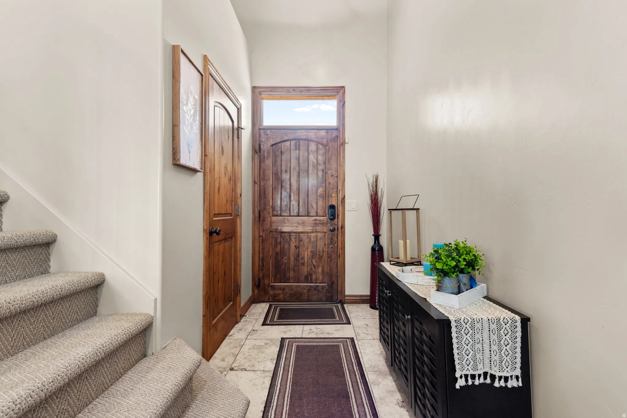 Foyer featuring a wood-panel entry door with transom window, stone-tile flooring, wood-panel interior door, and carpeted stairs