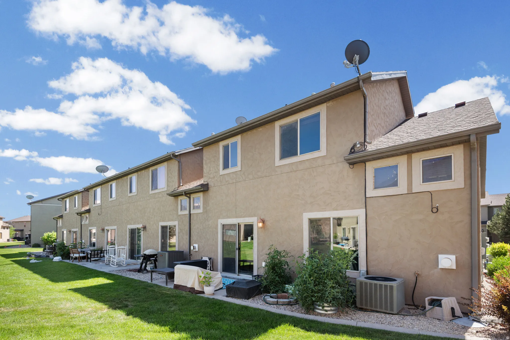 Rear exterior featuring stucco siding, multiple windows, sliding glass doors, and individual patio spaces