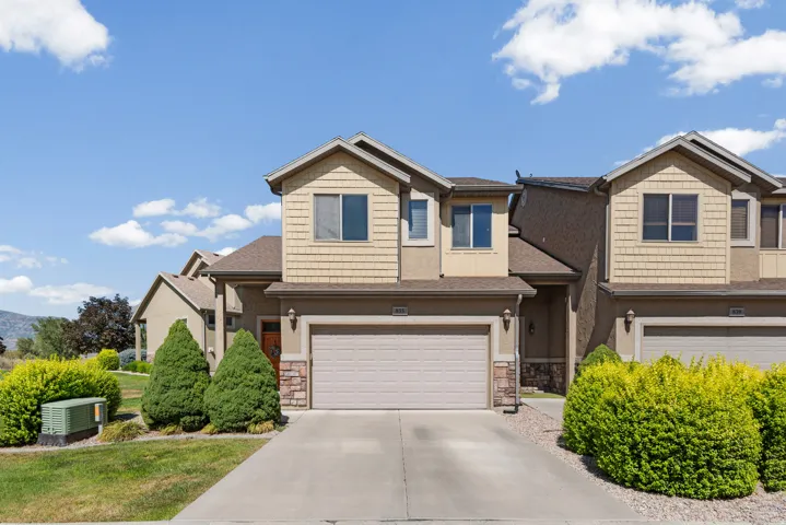 Multi-level exterior featuring tan siding, stacked stone accents, a beige garage door, and a concrete driveway