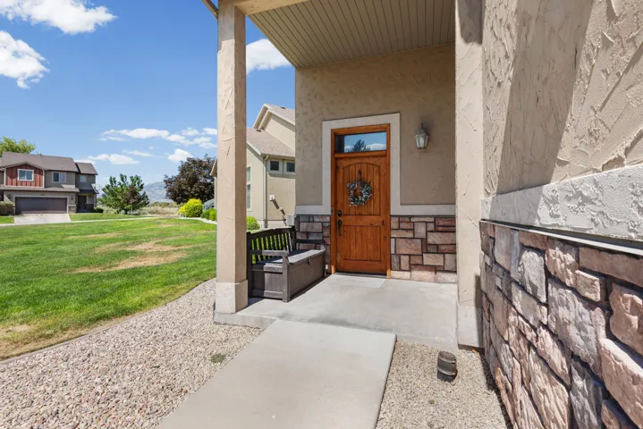 Inviting entryway featuring a wooden front door, stone veneer accents, stucco siding, and a covered porch with column supports