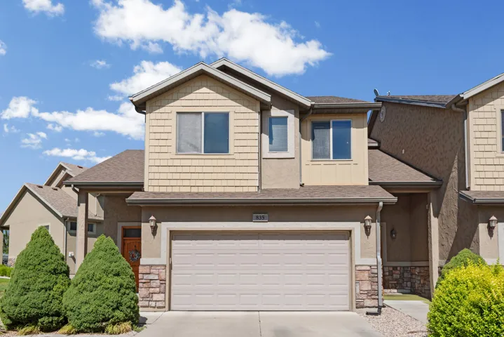 Two-story exterior featuring a neutral stucco and wood-shingle facade, a two-car garage, and a covered entry with a wood door