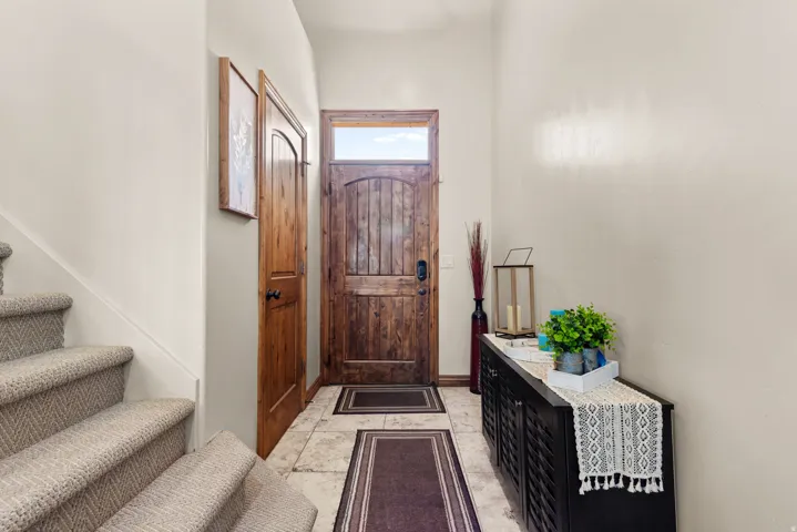 Foyer featuring a wood-panel entry door with transom window, stone-tile flooring, wood-panel interior door, and carpeted stairs