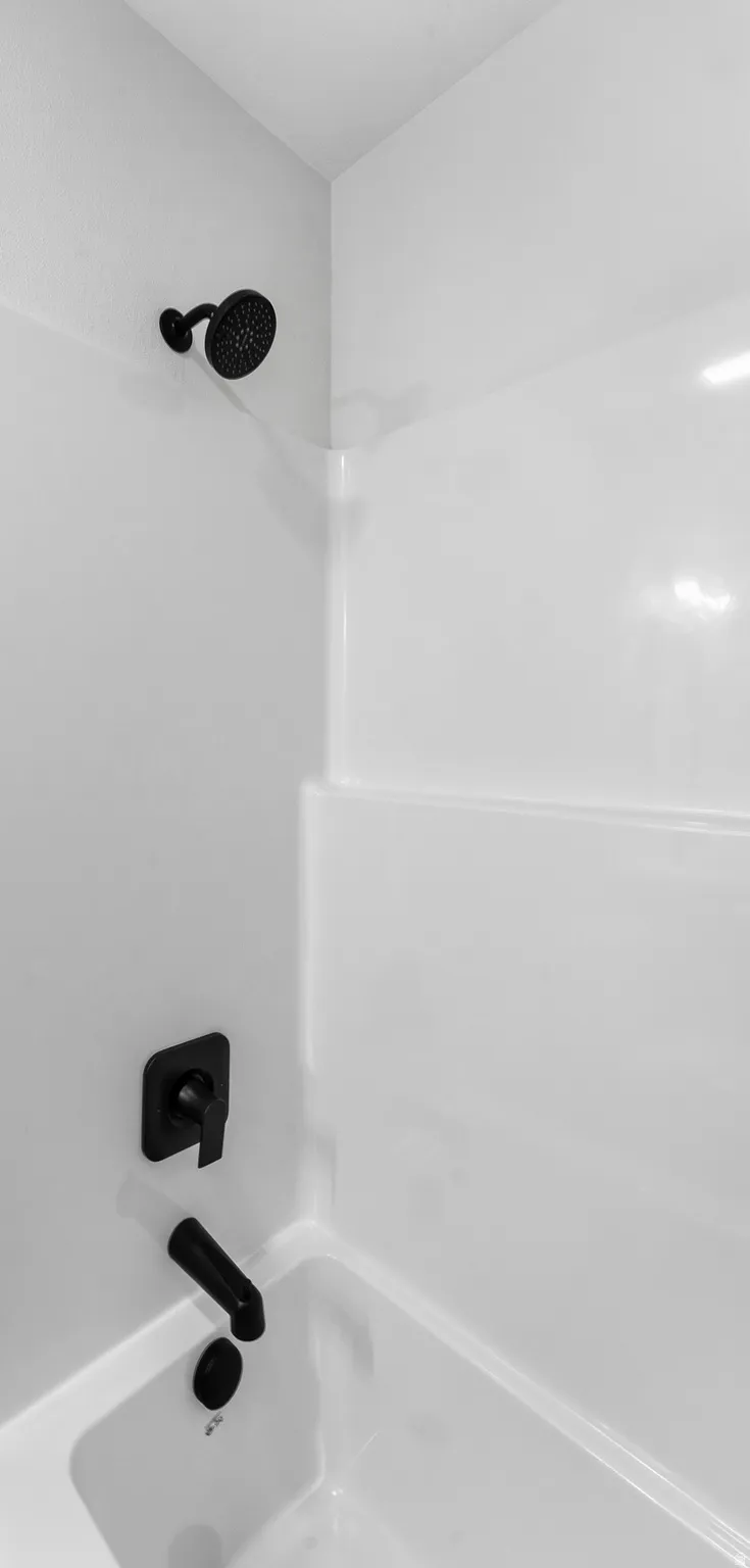 Bathtub and shower combination featuring a white surround, matte black shower head, and coordinating matte black tub filler with control handle