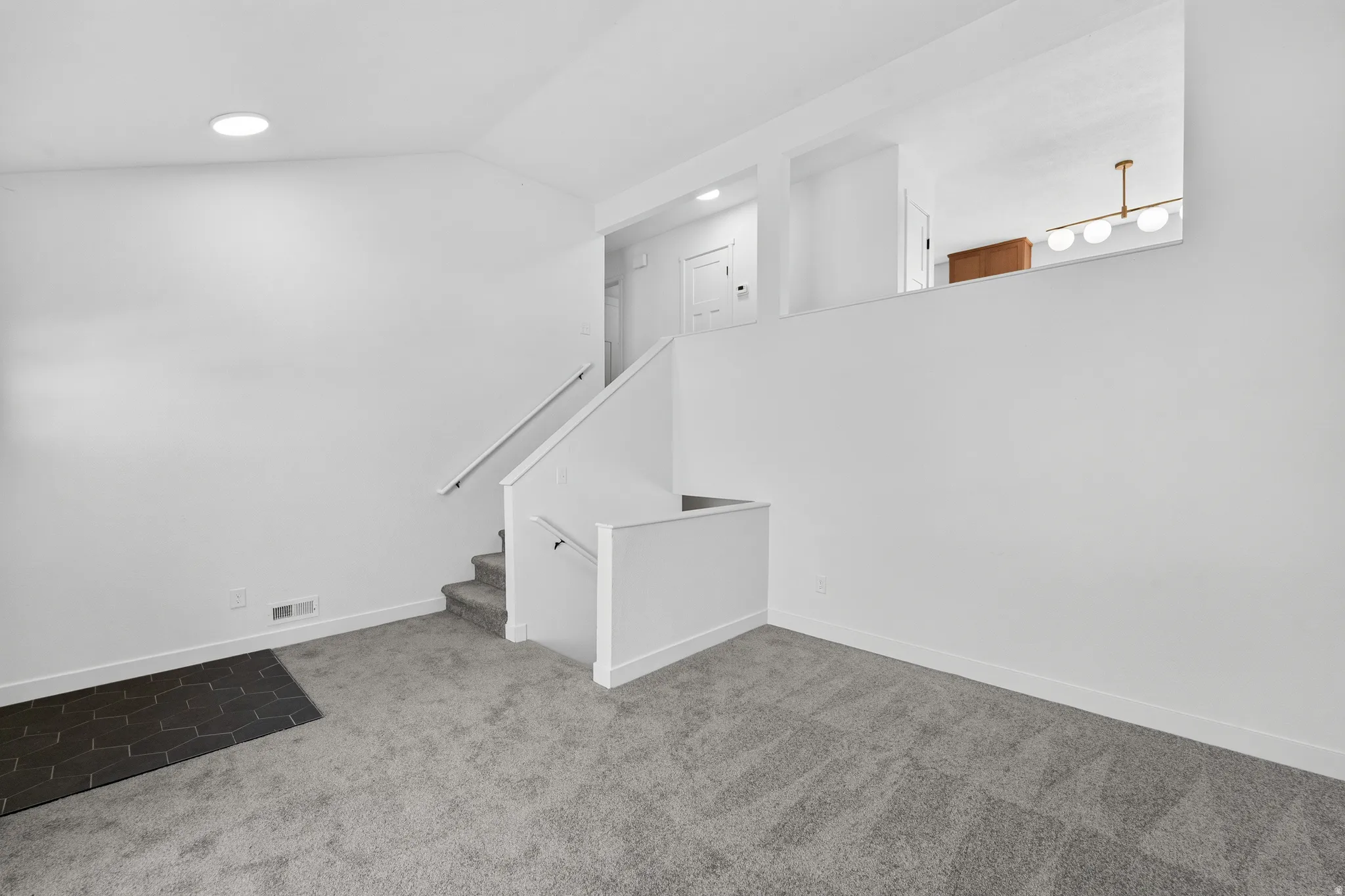 Spacious carpeted living area featuring white walls, recessed ceiling lighting, and a staircase with white railings