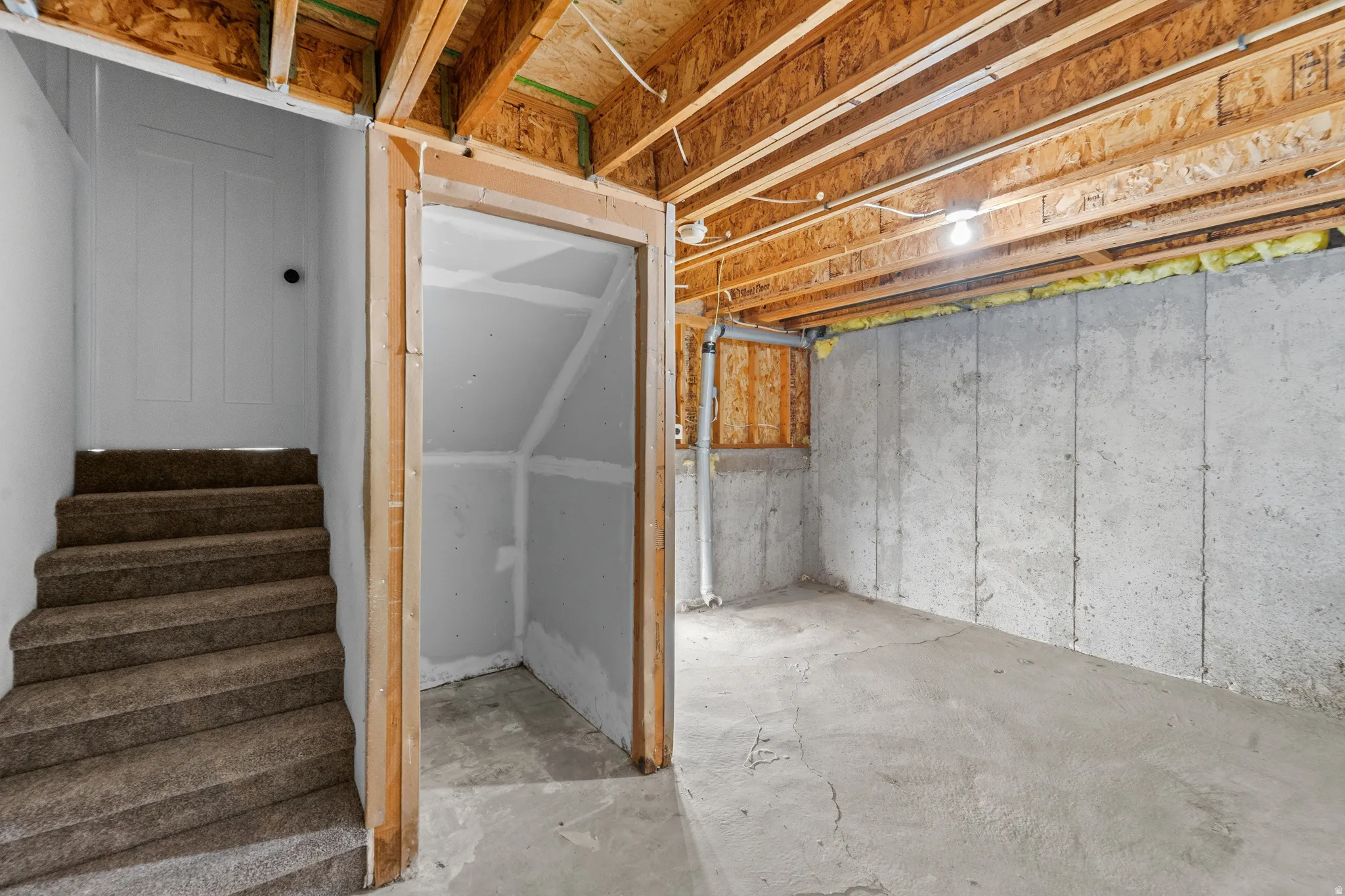 Unfinished basement space featuring exposed wooden ceiling joists, concrete walls, and concrete flooring