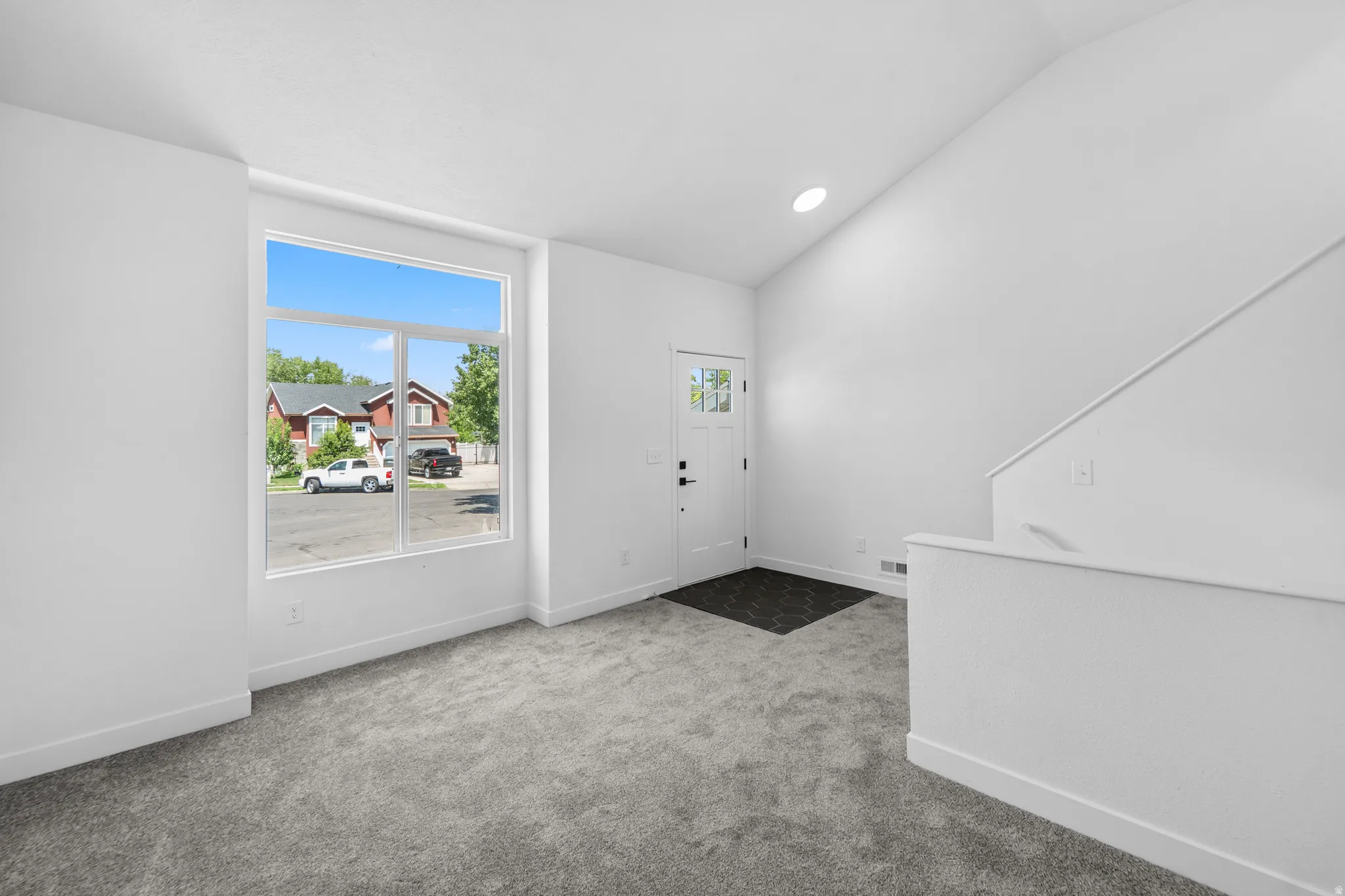 Bright living space featuring a large picture window, vaulted ceiling, and new gray carpet