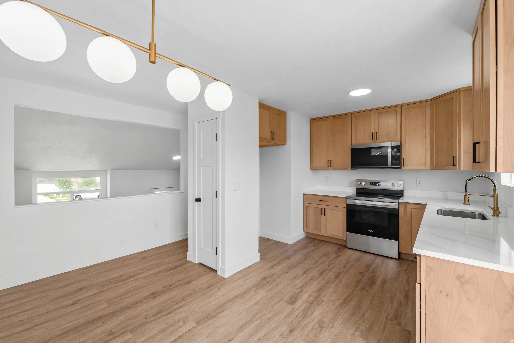 Modern kitchen featuring wood-finish flooring, light wood cabinetry, stainless steel appliances, white countertops, and a contemporary linear light fixture