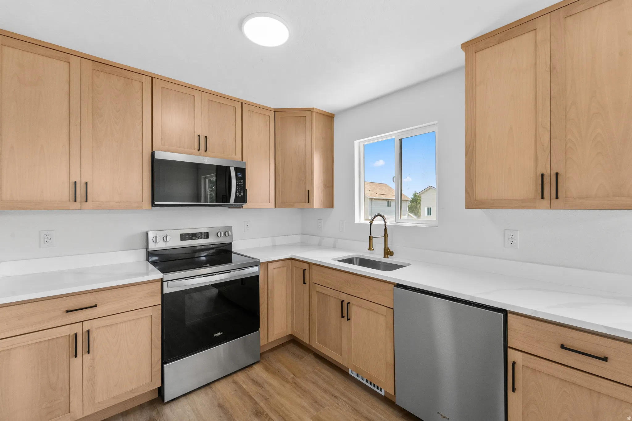Modern kitchen featuring light wood-finish cabinetry, stainless steel appliances, white countertops, and wood-finish flooring