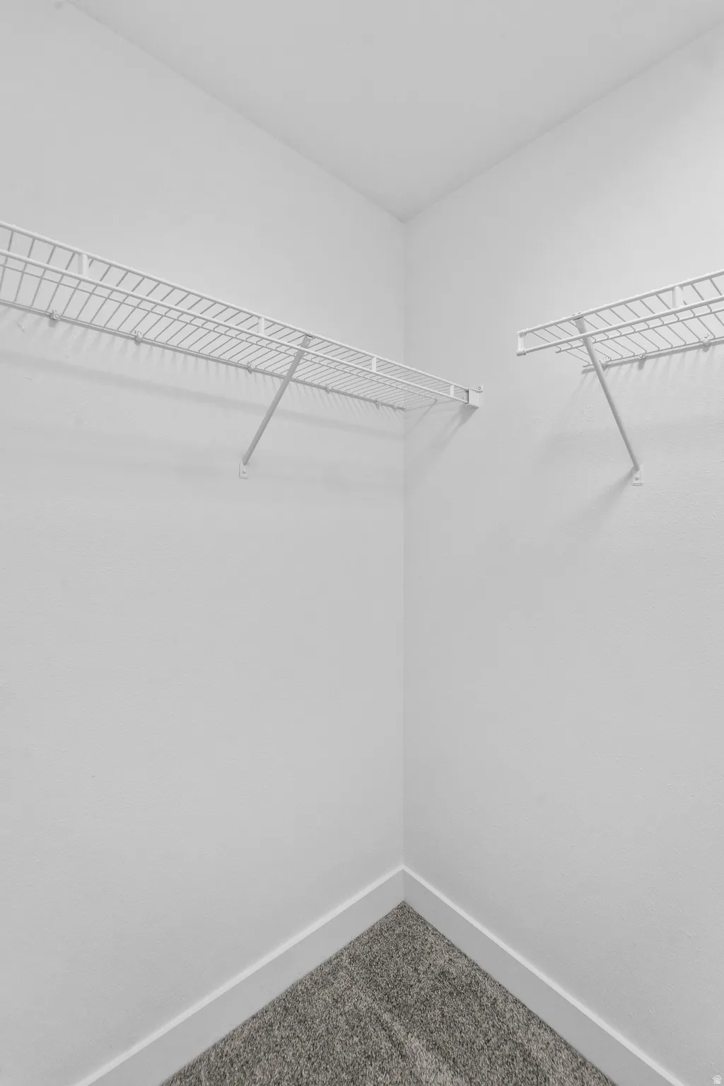 Corner closet with white wire shelving, white walls, and gray carpet flooring