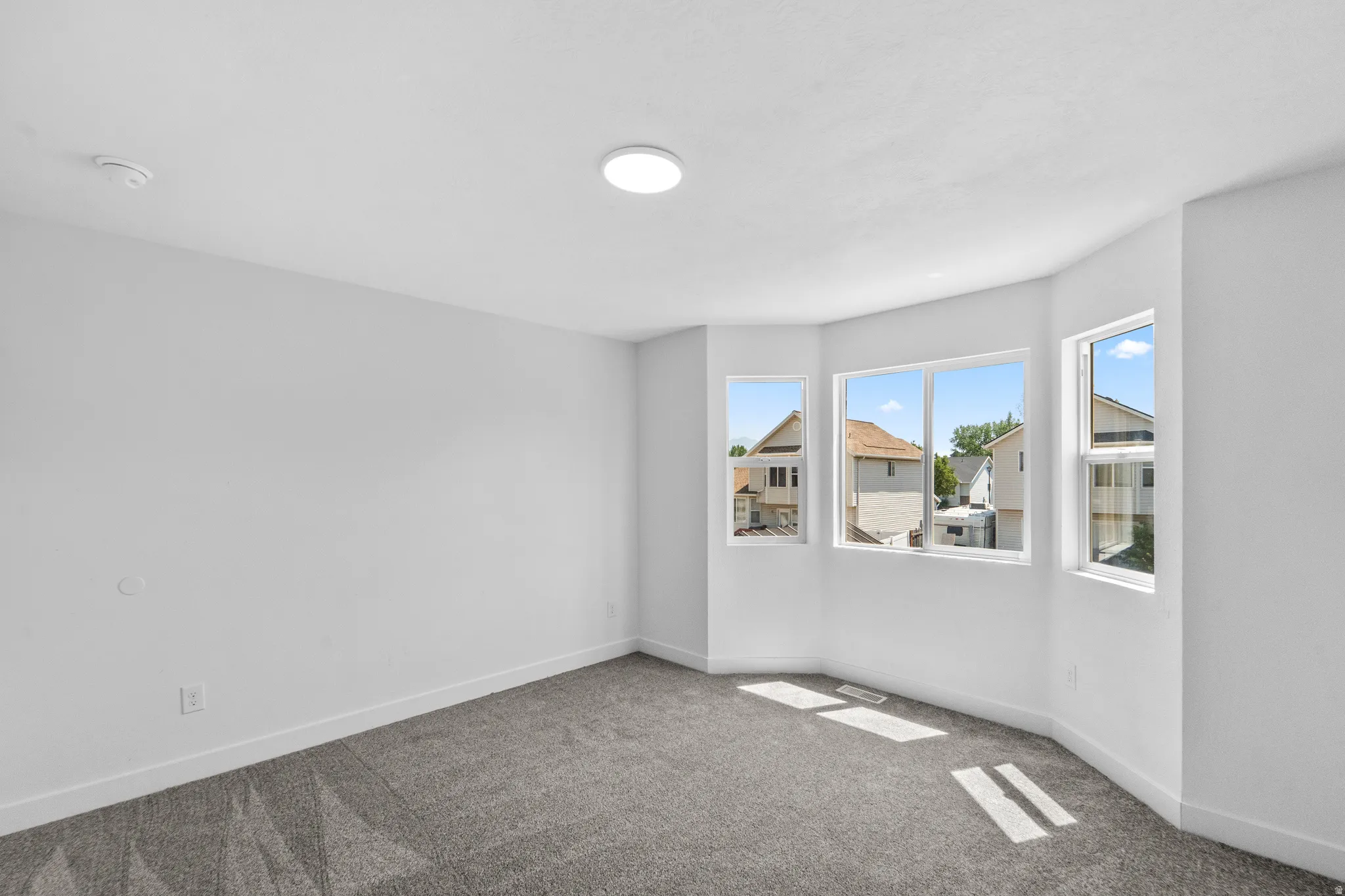 Bright corner bedroom with abundant natural light from multiple windows, neutral wall finishes, and soft-toned carpet flooring