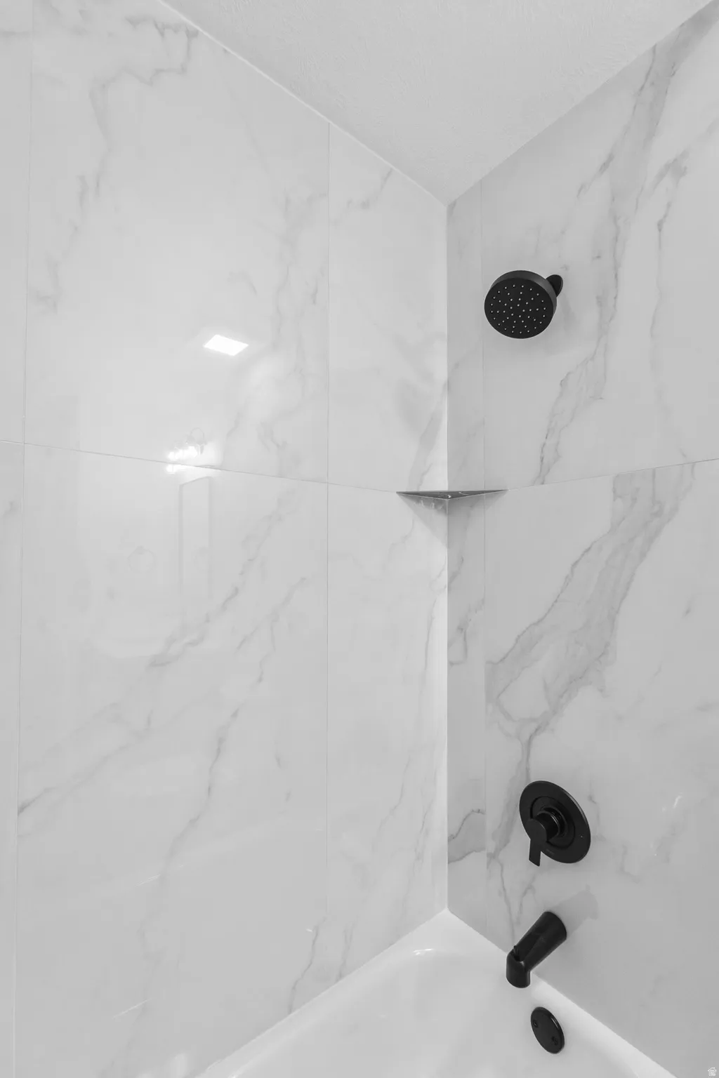 Bathtub and shower combination featuring white marble-look wall tiling, a matte black shower head, and coordinating matte black tub filler and control