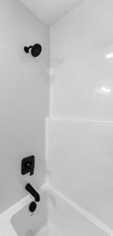 Bathtub and shower combination featuring a white surround, matte black shower head, and coordinating matte black tub filler with control handle