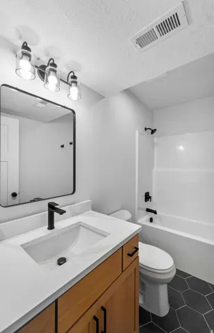 Bathroom featuring a wood-finish vanity with a white countertop, an undermount sink, and matte black fixtures