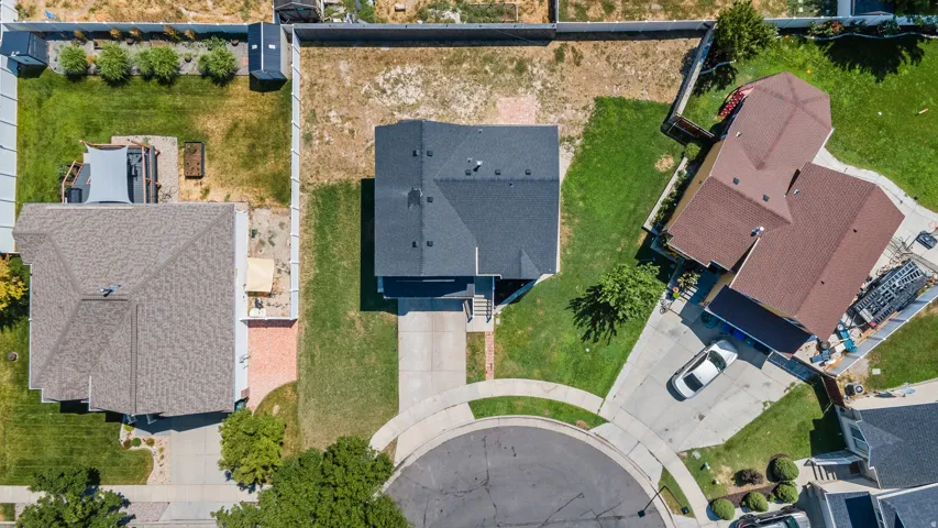 Overhead view showcasing a single-family residence with a dark shingle roof, a concrete driveway, and a partially grassed lot