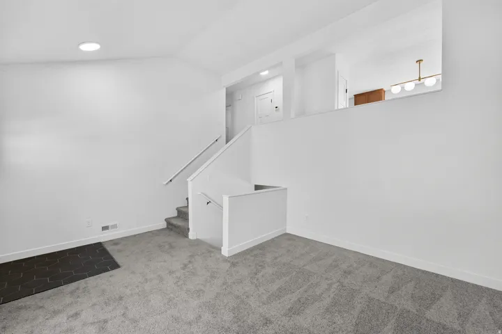 Spacious carpeted living area featuring white walls, recessed ceiling lighting, and a staircase with white railings