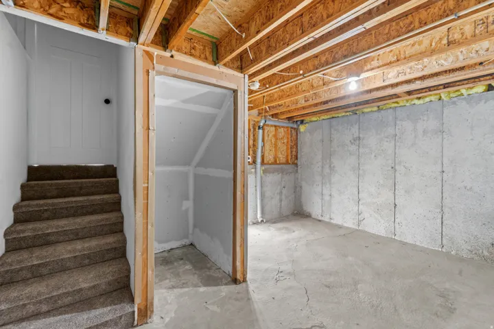 Unfinished basement space featuring exposed wooden ceiling joists, concrete walls, and concrete flooring