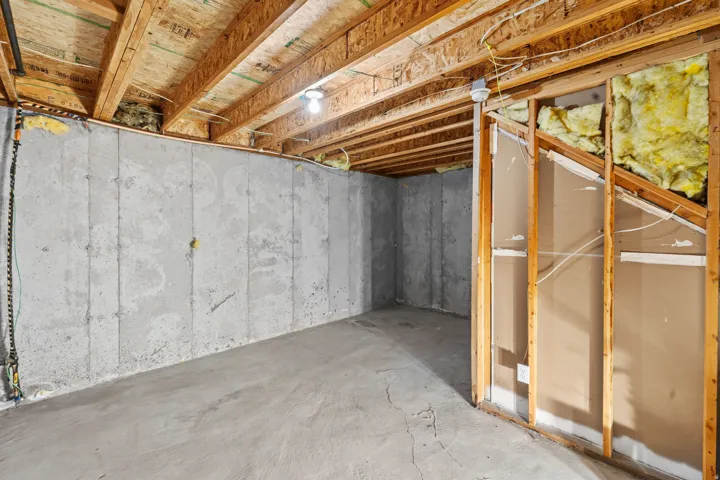 Unfinished basement area featuring poured concrete walls and floor, exposed wood joists, and existing framing with insulation