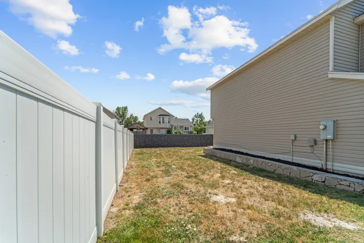 Private side yard featuring a vinyl privacy fence, tan siding, and a stone-edged planting bed