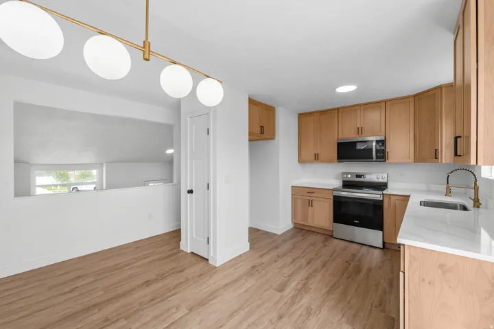 Modern kitchen featuring wood-finish flooring, light wood cabinetry, stainless steel appliances, white countertops, and a contemporary linear light fixture
