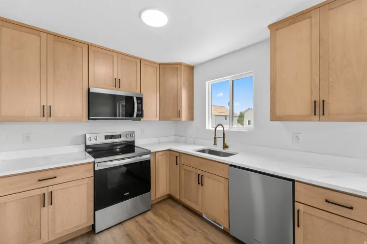 Modern kitchen featuring light wood-finish cabinetry, stainless steel appliances, white countertops, and wood-finish flooring