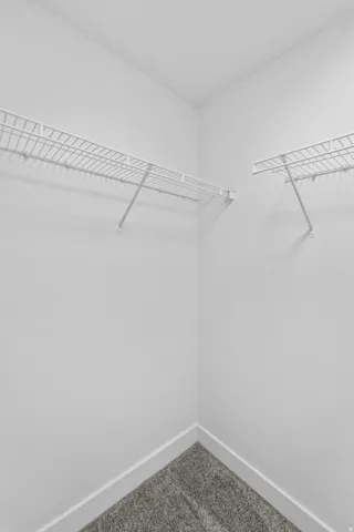 Corner closet with white wire shelving, white walls, and gray carpet flooring