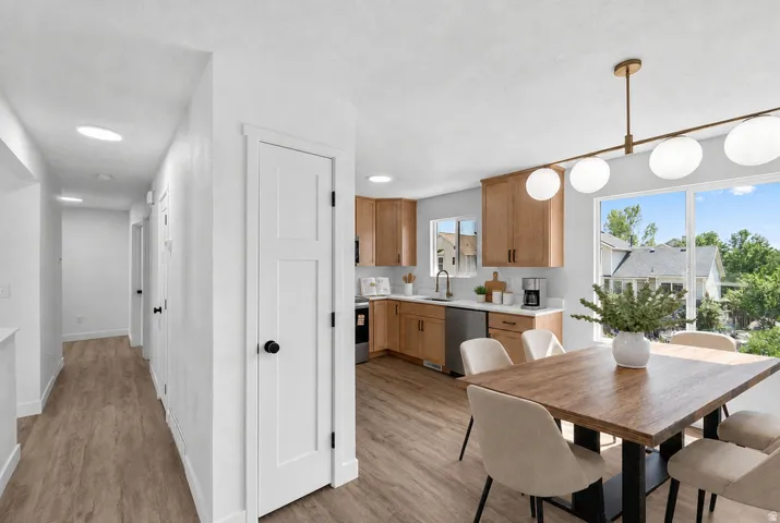 Open-concept kitchen and dining area featuring wood-finish flooring, custom cabinetry with warm wood tones, stainless steel appliances, quartz countertops, pendant lighting, and a wood dining table with upholstered seating