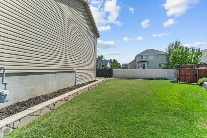 Spacious exterior featuring a large grassy yard, stone-lined landscaping bed with mulch, and full privacy fencing