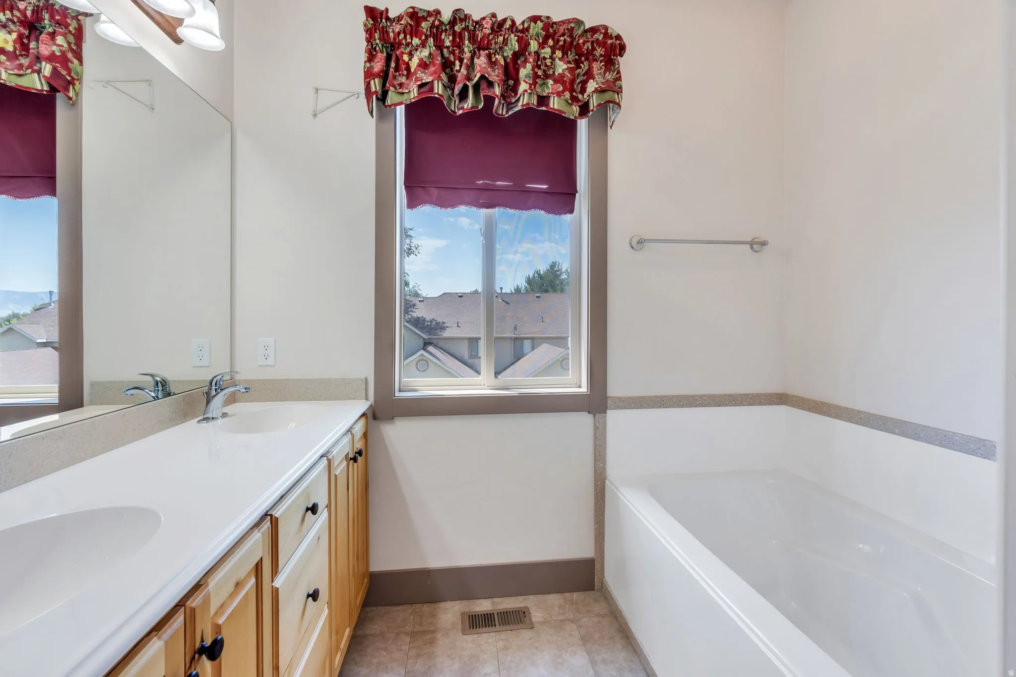 Bathroom featuring a double vanity with light wood cabinetry, a built-in bathtub, and a window