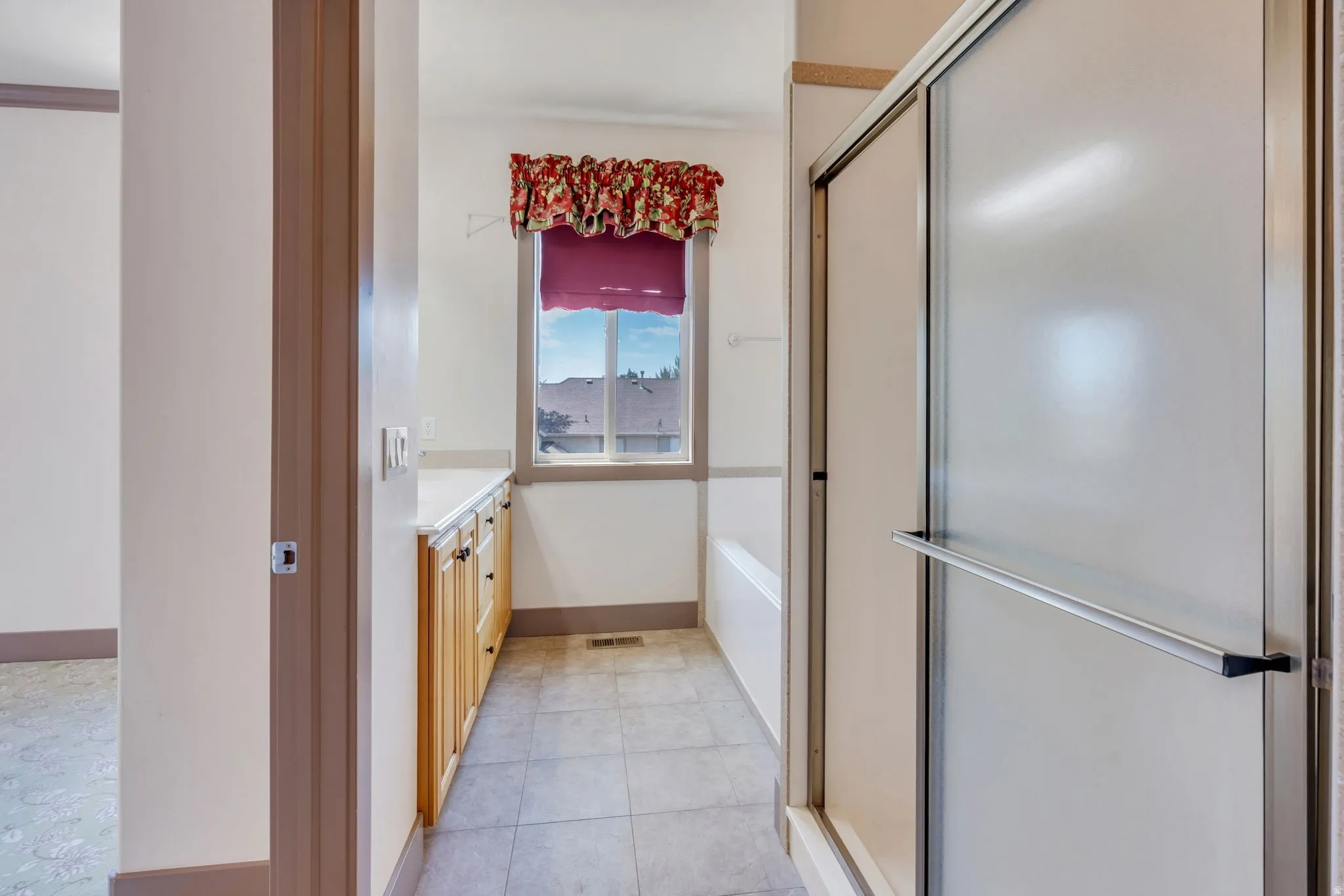 Bathroom featuring a shower enclosure with sliding door, a built-in bathtub, and a window with a valance